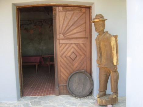 Vhod v Sosesko zidanico. Ker v Drašičih prirejajo tudi likovne kolonije, imajo kar nekaj umetniških del kot je ta leseni kip ob vhodu.